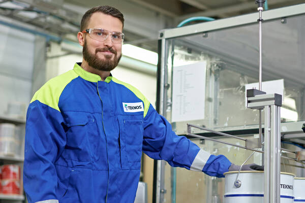 Teknos expert in safety gear inspecting a large white paint container in an industrial setting.