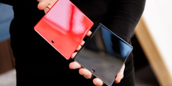 Person holding two metal samples with glossy coatings, one painted red and the other painted black.