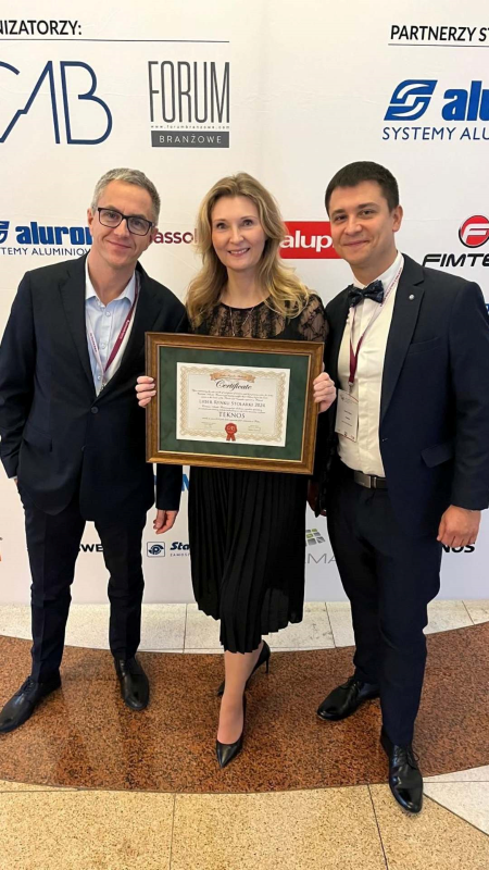 Marcin Radzinzki, Ilona Szczyrek, and Robert Udziela proudly holding an award certificate at the Windsor Hotel in Jachranka, standing in front of a sponsor-branded backdrop.