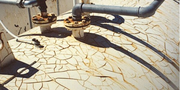 Surface of an industrial tank with cracked and peeling paint, showing signs of rust and weathering.