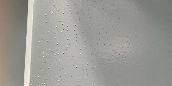 Close-up of a light gray painted surface with small blistering bubbles indicating coating defects.