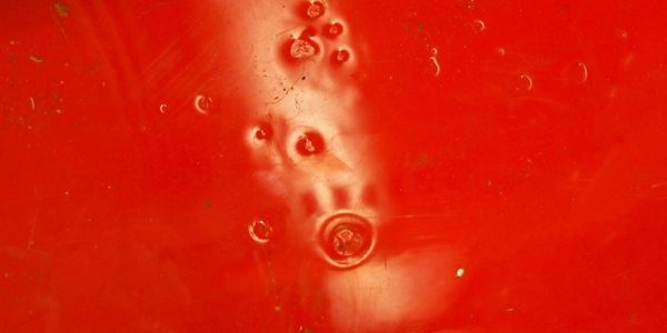 Close-up of red painted surface with small imperfections, fisheyes and bubbles.