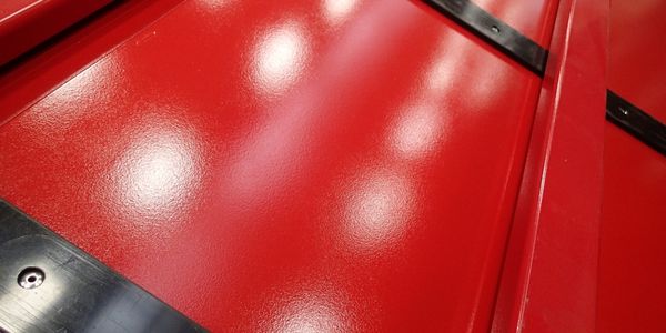 Close-up of a glossy red metal surface with reflections of overhead lights and uneven paint coverage.