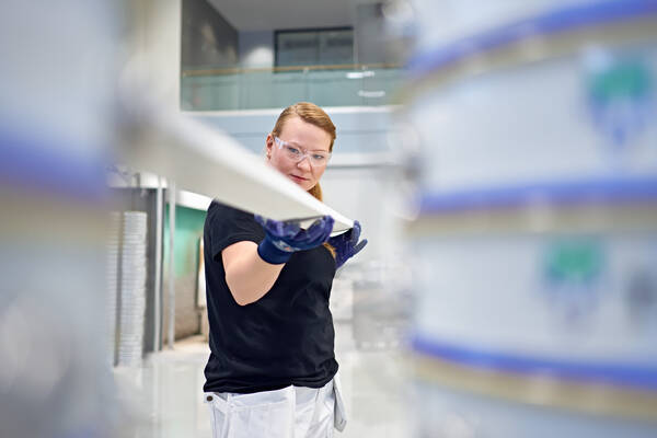 Industrial worker inspecting production line equipment while wearing protective gloves and glasses, focusing on quality control in a factory environment.