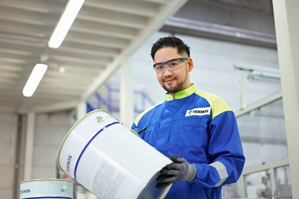 An expert in safety gear inspecting a large white paint container, focusing on quality control in an industrial environment.