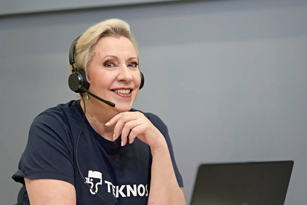 Teknos customer service representative smiling while wearing a headset, ready to assist customers, with a laptop in the background.