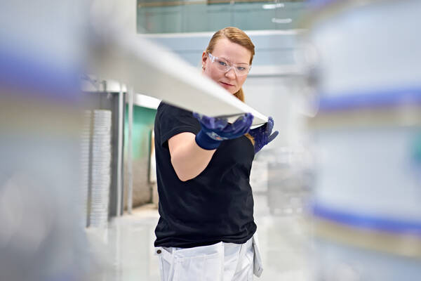 Teknos expert wearing safety glasses and gloves, inspecting a coated metal piece in a factory environment.