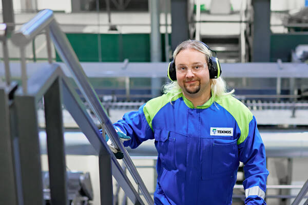 Teknos expert wearing protective gear and ear protection, standing on industrial stairs in a factory setting.