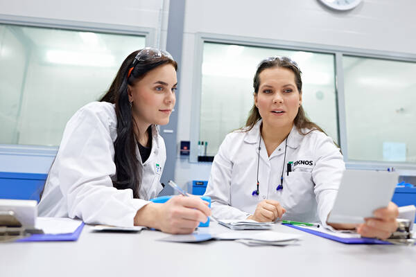 Two Teknos laboratory experts in lab coats reviewing paint samples and discussing results in a laboratory setting.